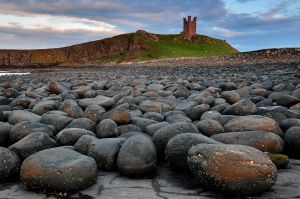 The late setting suns blasts Dunstanburgh Castle and the boulders